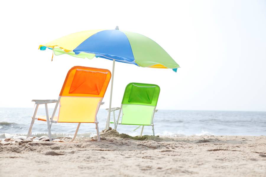 Orange and green beach chairs under a colorful beach umbrella on a seashore